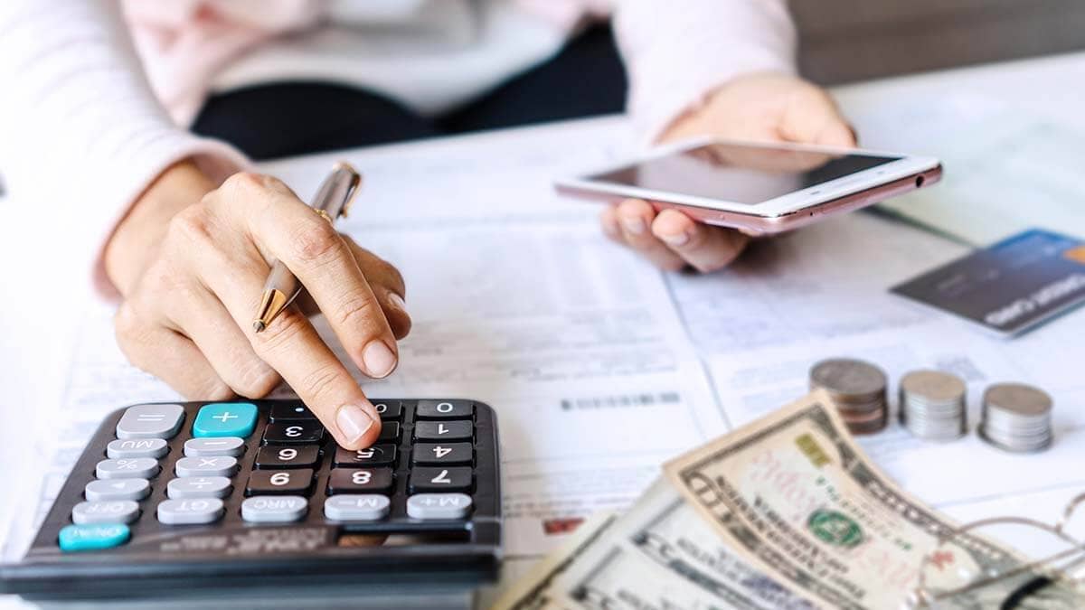 Calculator, cell phone, paperwork, and money on a work desk.