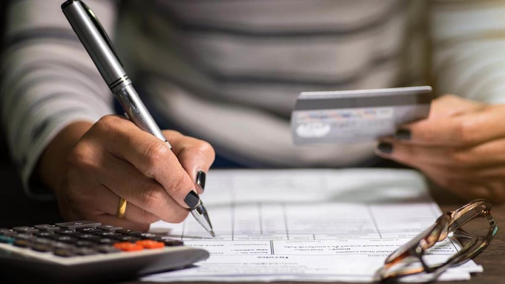 Woman holding credit card and writing on paper.