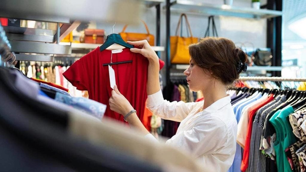 Woman in a clothing store looking at the price on a red dress.