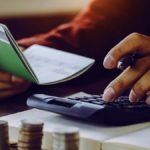 Hands on a calculator and holding a notebook.