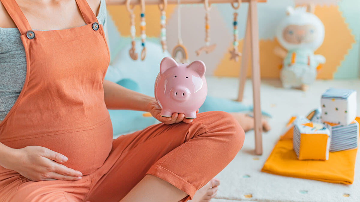 Pregnant woman holding a pink piggy bank.