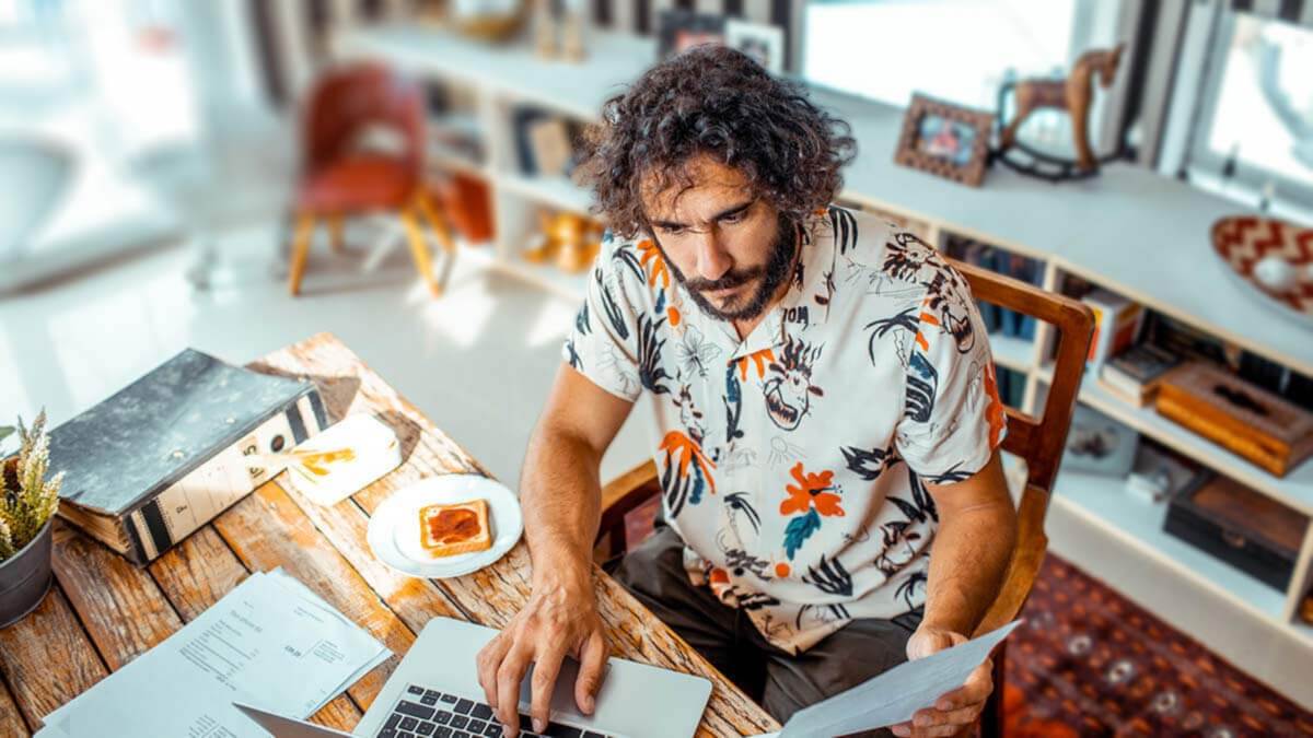 Aerial view of a man using a laptop and holding a piece of paper.