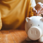 Woman putting a coin into a white piggy bank.