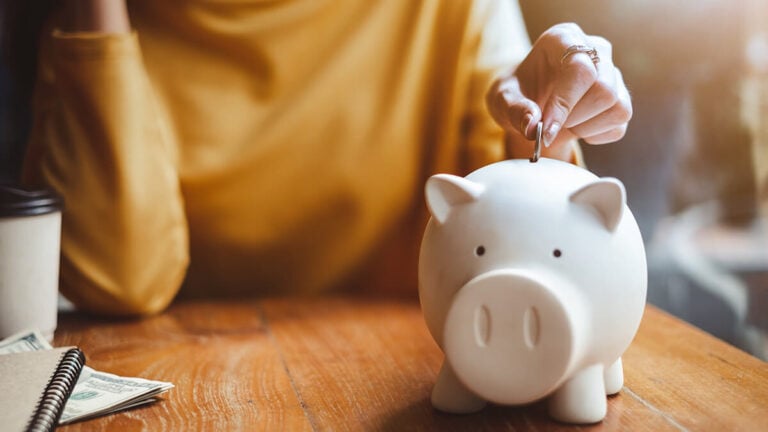Woman putting a coin into a white piggy bank.