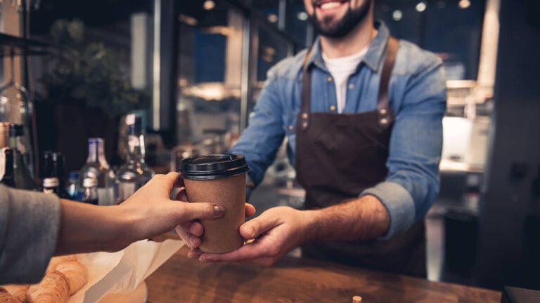 Barista handing a to-go coffee to a customer.