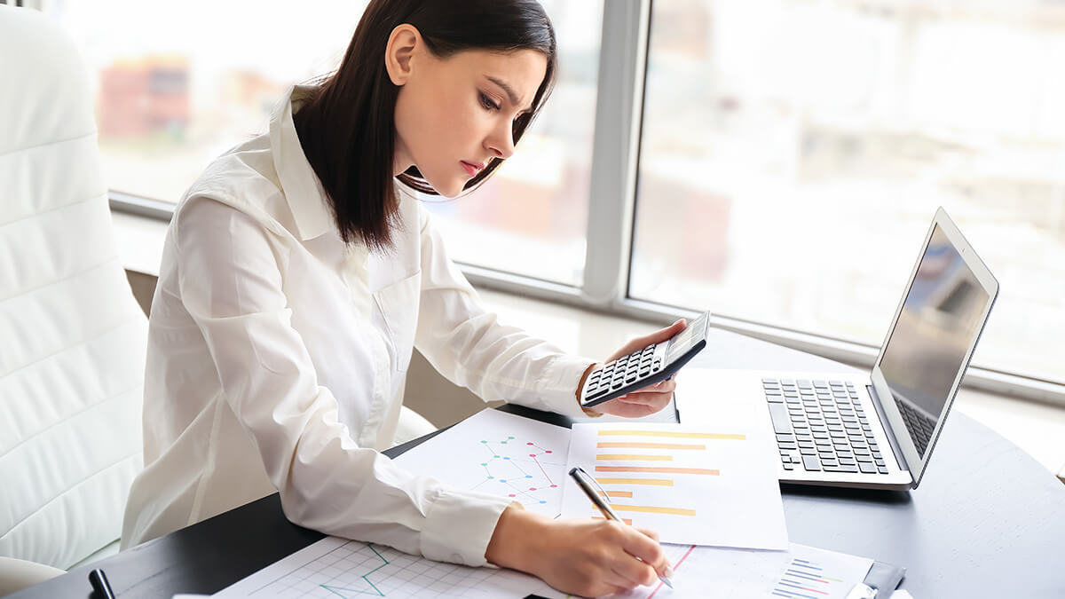 Woman filling out paperwork with the help of a calculator.