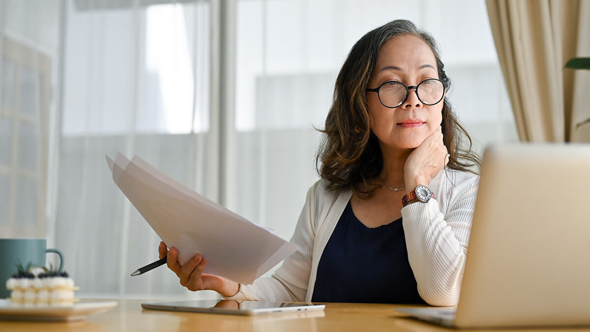 Woman with hand on neck, looking at laptop.