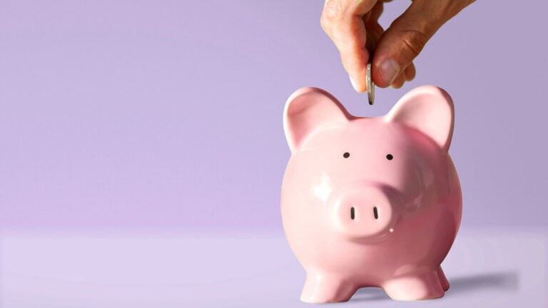 Hand putting a coin in a piggy bank.