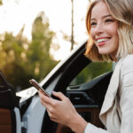 Woman stepping out of her car logging her business use of vehicle in her cell phone.