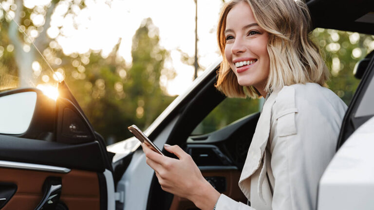 Woman stepping out of her car logging her business use of vehicle in her cell phone.