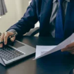 Business tax attorney using the laptop and looking at a document.