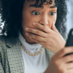 Shocked business owner looking at tax scams on her phone.