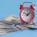 Pink clock on fanned out $100 bills.