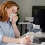 Employee blowing her nose at her desk.