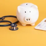 Piggy bank, stethoscope, and calculator on a yellow background.