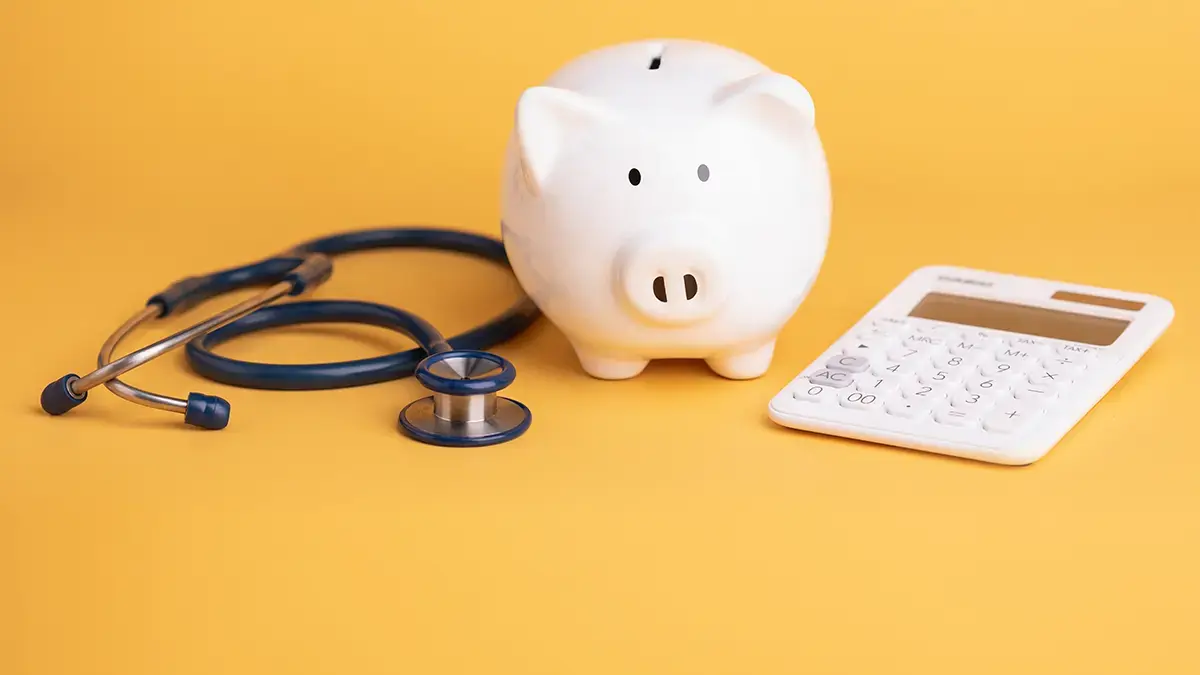 Piggy bank, stethoscope, and calculator on a yellow background.