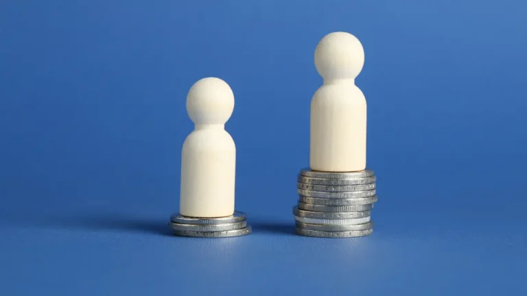 Wooden figures standing on coin stacks of varying heights, illustrating differing employee pay levels and pay compression.