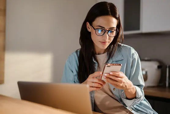 Woman comparing payroll software using phone and laptop