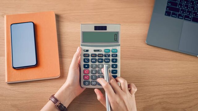business owner using a calculator and income tax withholding tables to determine federal income tax withholding